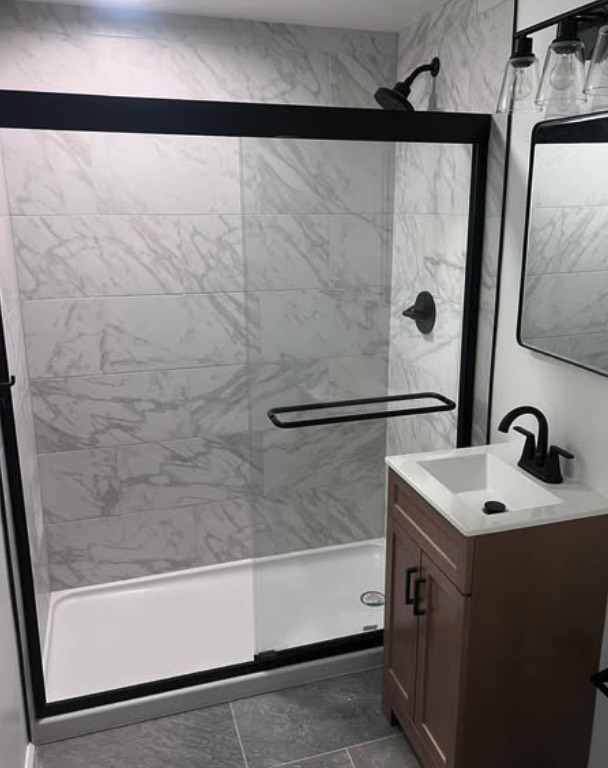 Remodeled bathroom with frameless glass shower, marble-look tile, and matte black fixtures