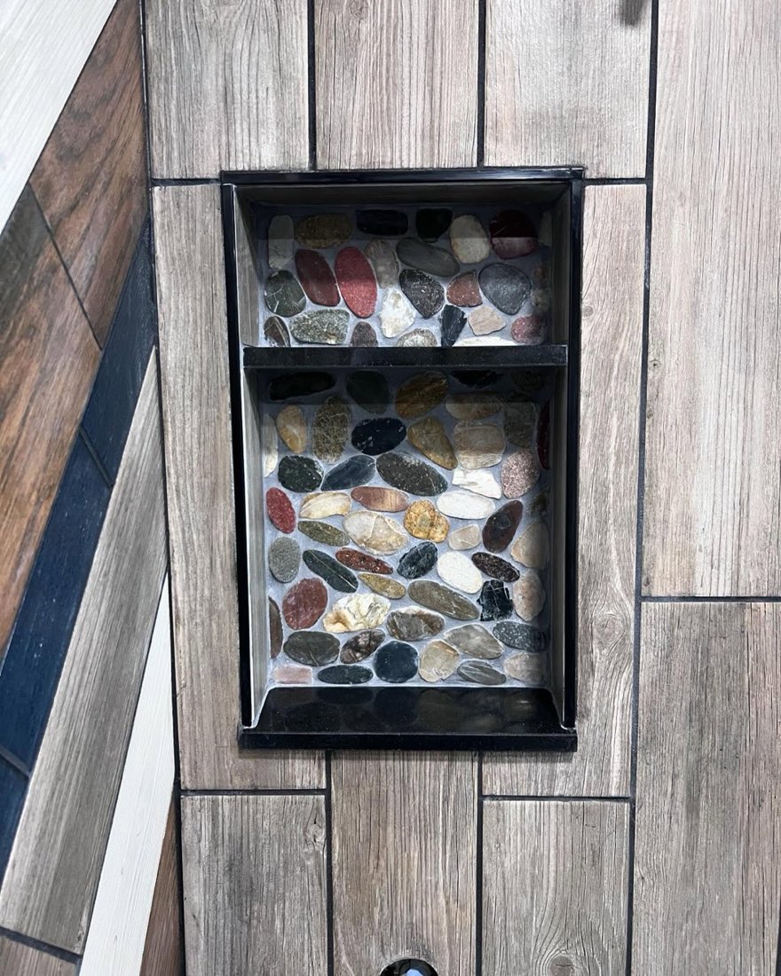 Modern farmhouse shower detail with wood-look tile and river-pebble mosaic niche