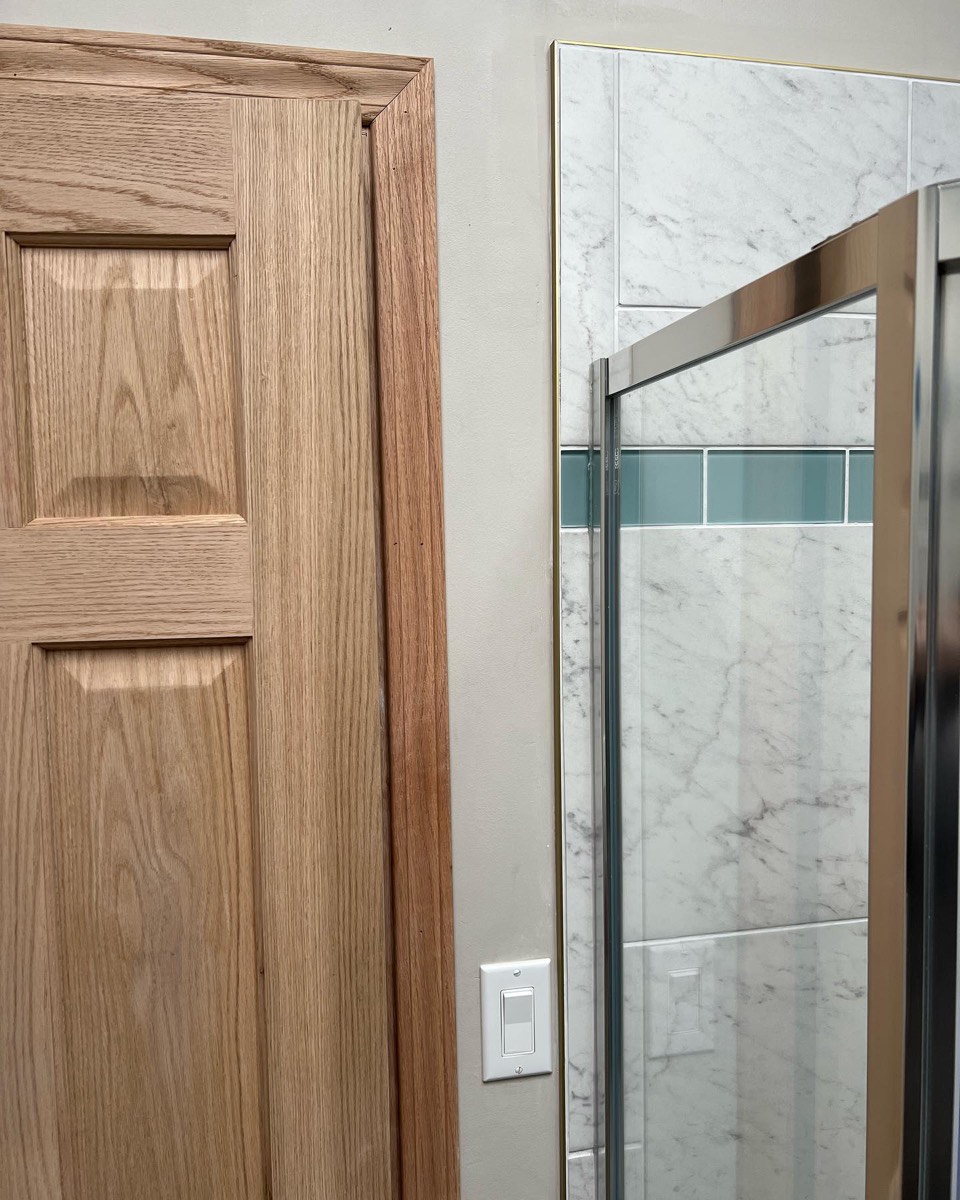 Bathroom renovation detail with oak door and marble-tile shower with teal accent band