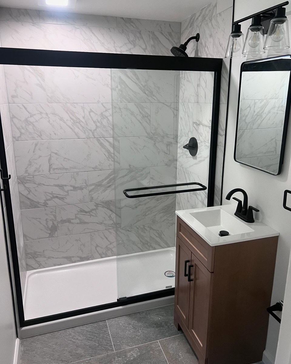 Bathroom remodel with marble-tile shower, black-framed glass door, and wood vanity