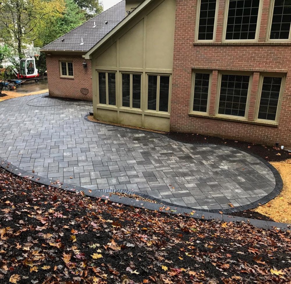 Large slate-toned paver patio with charcoal border wrapping a brick home