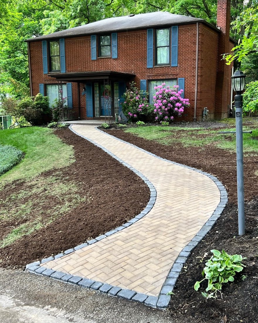 Curved Holland-paver front walkway with charcoal cobblestone border at a brick home