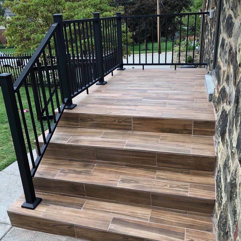 Rustic porch renovation with wood-look tile steps and black metal railing