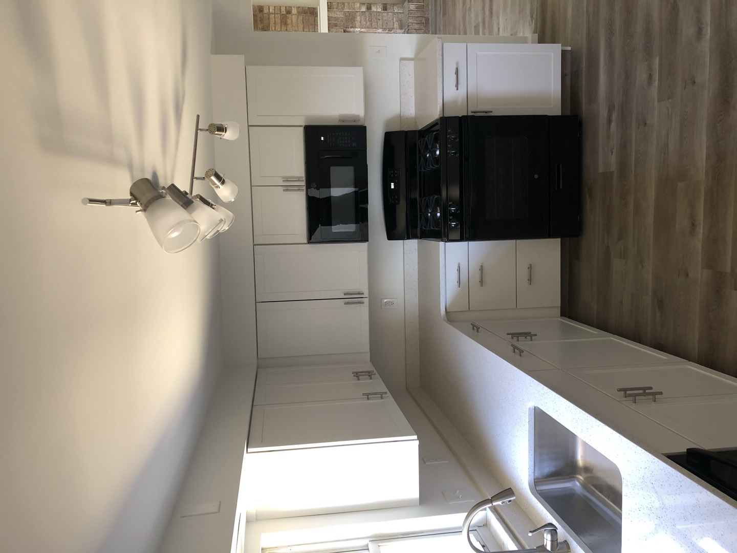 Remodeled kitchen with white shaker cabinets, speckled quartz countertops, and wood-look flooring